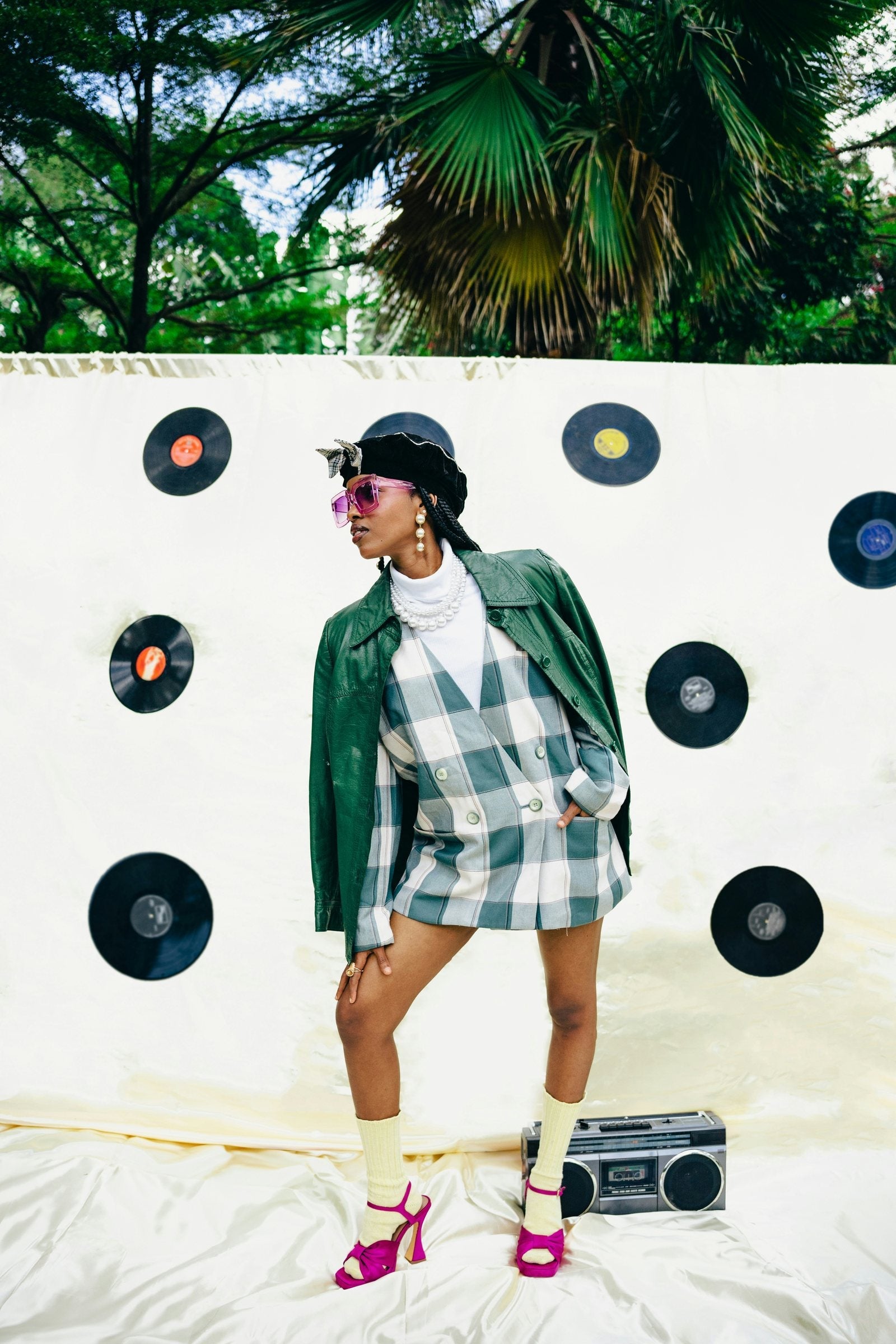 Editorial: retro look with plaid blazer, beret, pearls and pink sunglasses against a wall of vinyl records