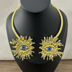 Gold necklace with eye design on a black mannequin against a neutral background