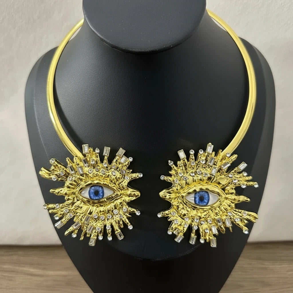 Gold necklace with eye design on a black mannequin against a neutral background