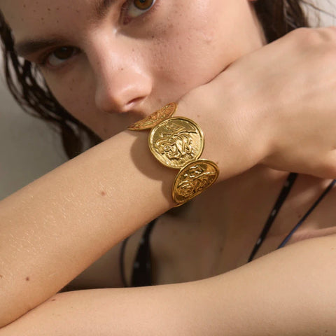 Close-up of a person wearing gold bracelets on a neutral background