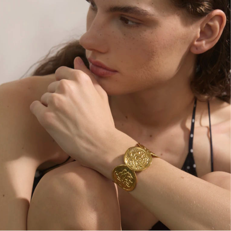 Woman wearing a gold bracelet with a neutral background