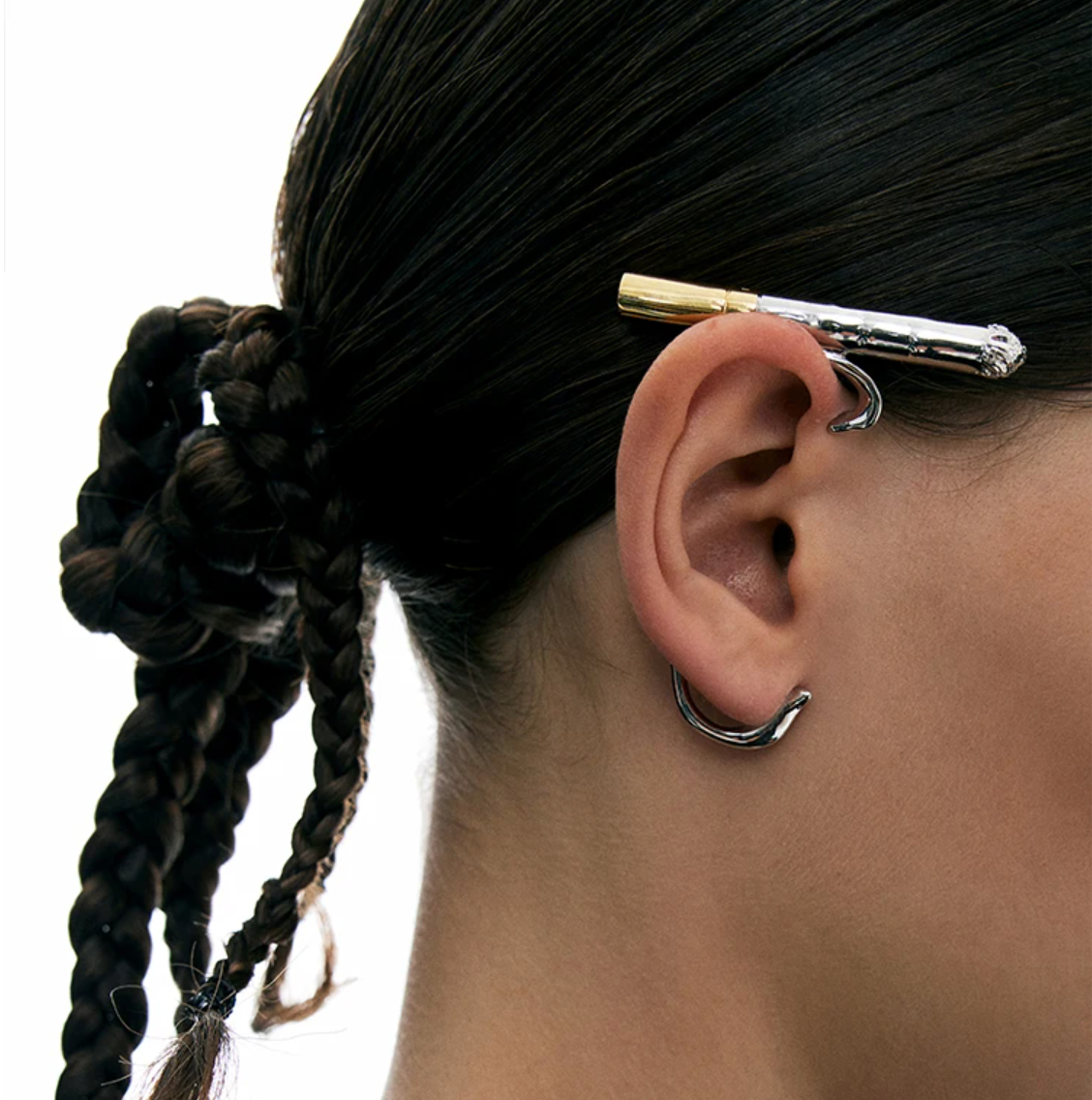 Person with braided hair wearing a silver earring ear cuff 