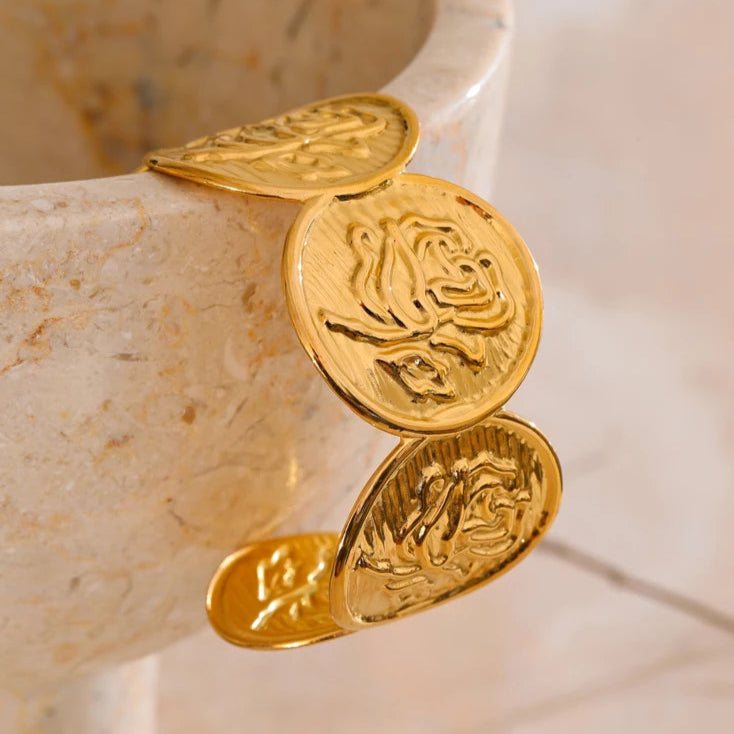 Gold bracelet with coin-like charms on a marble surface