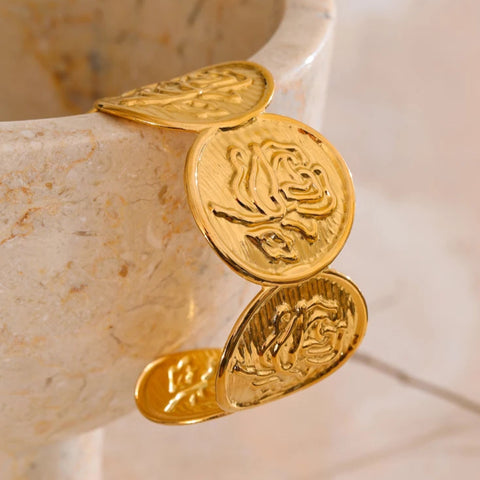 Gold bracelet with coin-like charms on a marble surface