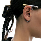 Close-up of an ear with metal cigarette ear cuff earrings and braided hair on a white background