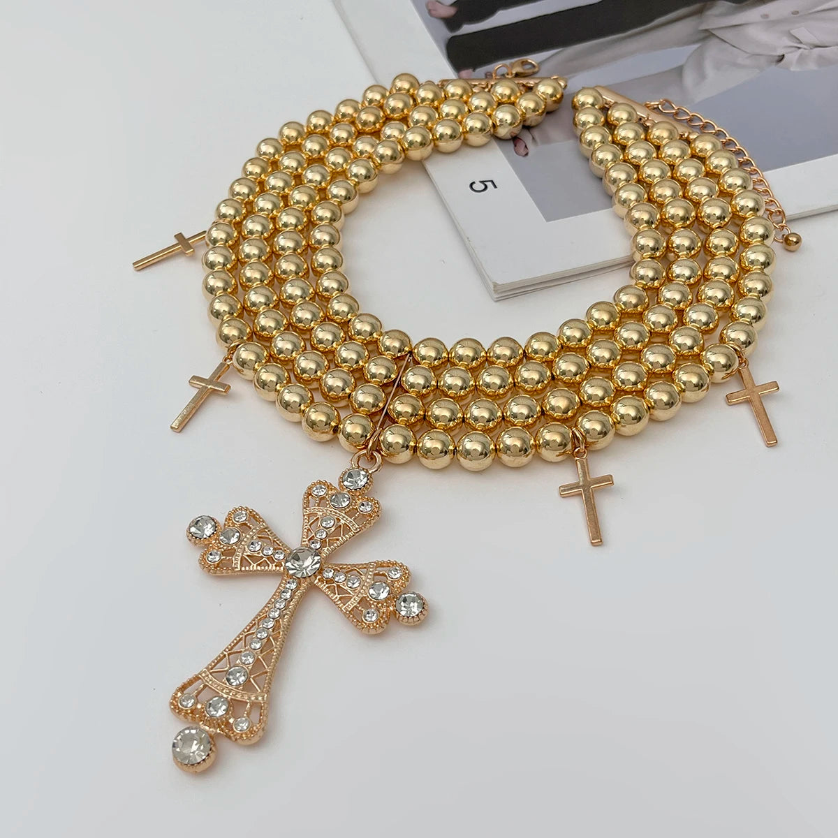 Gold beaded necklace with cross pendants on a white surface Image principale du produit