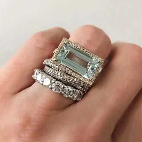 Two rings with gemstones on a hand against a neutral background