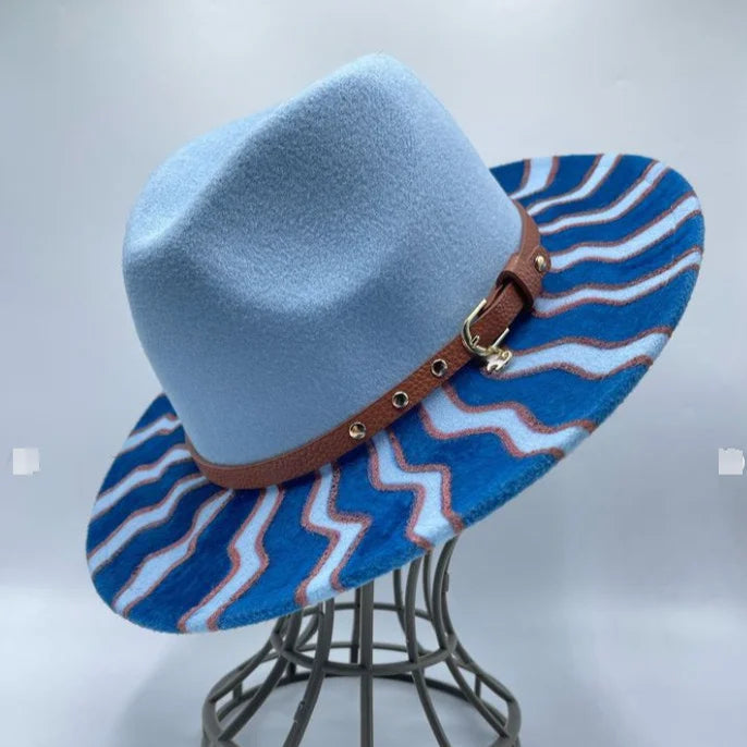 Blue fedora hat with a wavy patterned brim on a gray stand against a light gray background